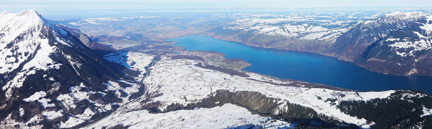 A panoramic view of a serene blue lake surrounded by snow-capped mountains under a clear sky.