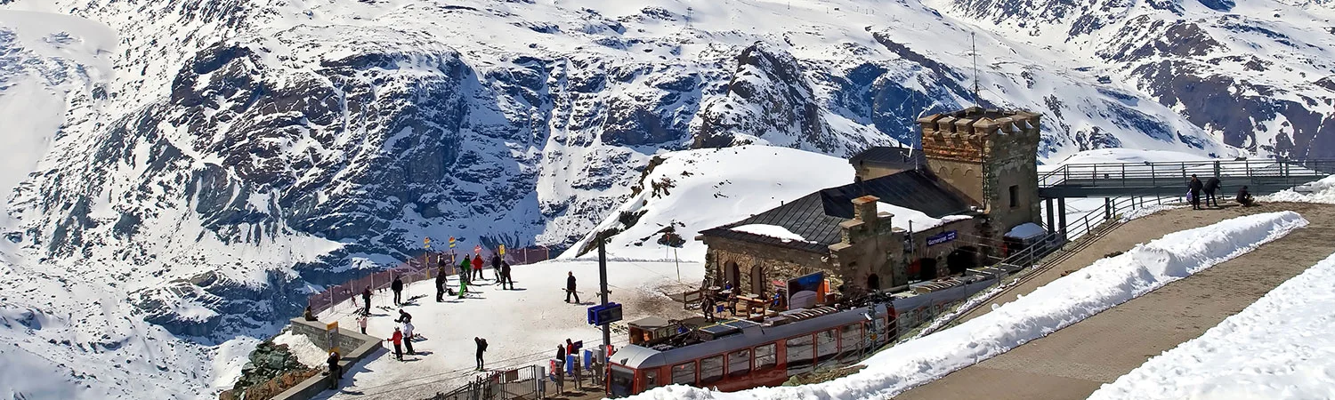 A sunny winter scene of  mountain resort with skiers, snowboarders, and a red train near a rustic building.