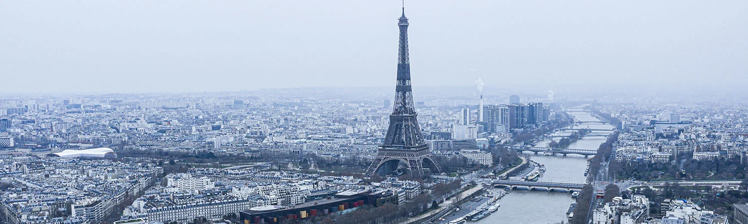 A panoramic view of Paris featuring the iconic Eiffel Tower standing prominently amidst the cityscape, bordered by the serene Seine River.