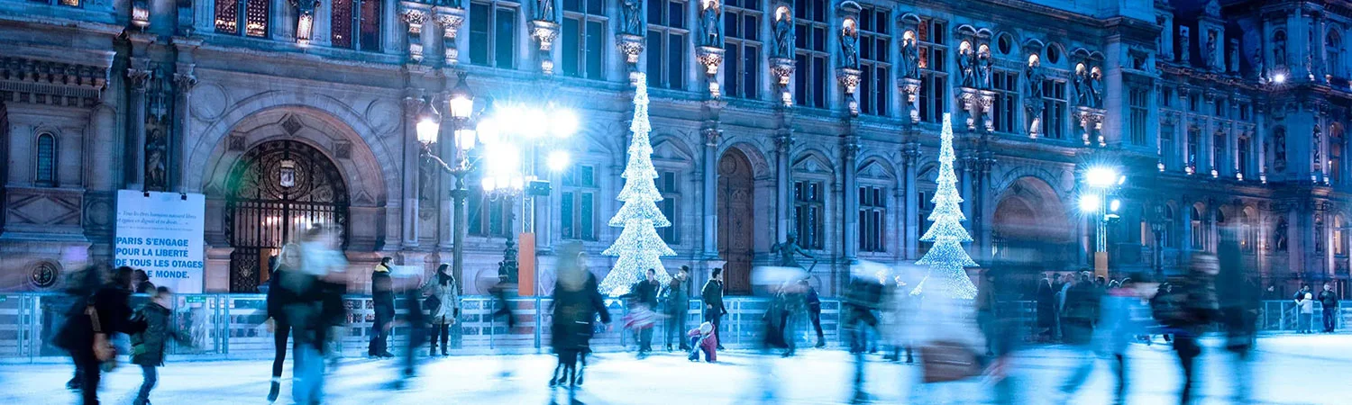 “People ice skating at night in front of a beautifully illuminated historic building, adorned with bright Christmas tree lights during the holiday season in Paris.”