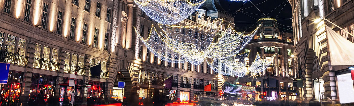 A festive night scene in a city with angel lights, decorated buildings, and people walking on the sidewalk. 