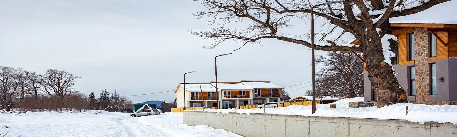 A snowy landscape featuring a modern residential building, bare trees, and a clear sky.